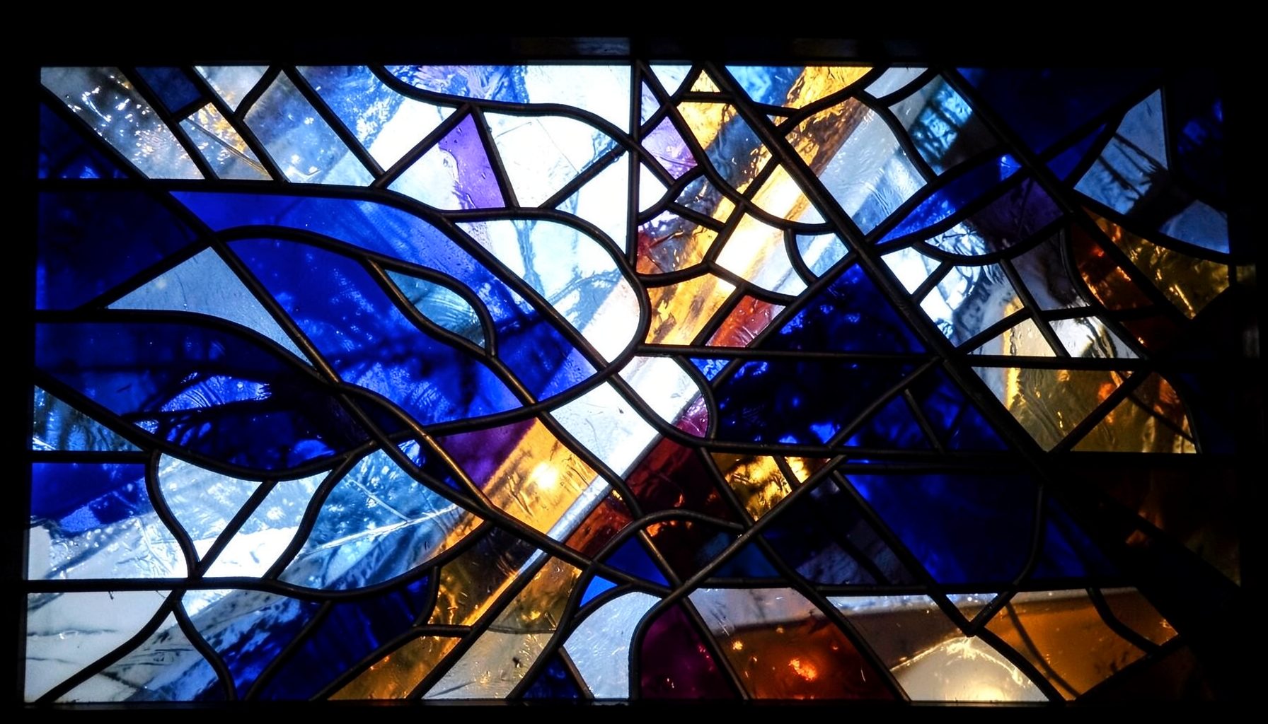 A dramatic stained-glass composition with bold leaded segments in deep blues, icy whites, and rich amber tones, evoking the speed and intensity of hockey under arena lights